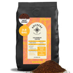 A 2lb bag of Kochere Coffee Company’s Colombian Medellin Single Origin Medium Roast, drip grind, with dried orange and berry notes, is shown with coffee grounds spilled in front.