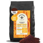 A 2lb bag of Kochere Coffee Company’s Costa Rican Alajuela Medium Light Roast, with sweet apple and raisin notes, sits labeled “fresh and roasted to order,” fine grounds scattered in front.