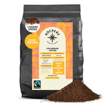 A 5 lb bag of Kochere Coffee Colombian Medellin Single Origin Medium Roast—dried orange and berry notes, coarse grind. Fresh grounds in front with detailed packaging and Fairtrade label from Kochere Coffee Company.