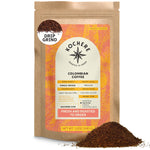 A brown bag of Kochere Coffee Company's Colombian Medellin Single Origin Medium Roast, with dried orange and berry notes, sits beside a pile of ground coffee. The label shows it's drip grind, fresh, and roasted to order.