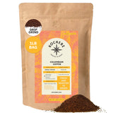 A 1-pound bag of Kochere Coffee Company’s Colombian Medellin Single Origin Medium Roast, with dried orange and berry notes in drip grind, shows product details on the label and a small pile of ground coffee in front. [1lb][drip grind]