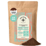 A 1lb bag of Kochere Coffee Ethiopian Sidamo Natural Medium-Light Roast by Kochere Coffee Company, with milk chocolate and fruity notes, stands upright with some coarse ground coffee gracefully spilled in front.