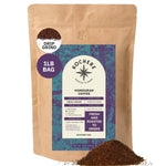 A 1 lb bag of Kochere Coffee Company Honduran Marcala Organic Medium Roast—notes of caramel, spice, and brown sugar—in beige and purple packaging. Loose organic coffee grounds are displayed in front.