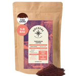 A 1lb bag of Kochere Coffee Company’s Tanzanian Mbeya AB Medium-Light Roast, featuring pear, floral, and jasmine notes, is freshly roasted to order with aromatic grounds shown in front.