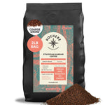 A 2lb bag of Kochere Coffee Ethiopian Harrar Natural Medium Roast sits with ground coffee spilled in front. The label notes fruity, berry, and dark chocolate flavors. Single origin, roasted to order by Kochere Coffee Company. Coarse grind shown. [2LB][coarse grind]
