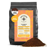 A 5lb bag of Kochere Coffee Colombian Medellin Single Origin Medium Roast, drip grind, with dried orange and berry notes; Fairtrade certified by Kochere Coffee Company. Ground coffee is piled in front. [5lb][drip grind]