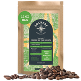 A 12 oz bag of Kochere Coffee Company's Safari "Coffee of the Month" Club sits upright with scattered beans, highlighting its fresh-roasted, single-origin whole beans—ideal for any coffee lover’s subscription.