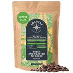 A 1LB bag of Kochere Coffee Company's Safari "Coffee of the Month" Club sits upright with scattered beans, highlighting its fresh-roasted, single-origin whole beans—ideal for any coffee lover’s subscription.[1LB][Whole Bean]