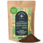 A 1 LB bag of Kochere Coffee Company’s Safari "Coffee of the Month" Club—Fresh Roasted Single Origin Subscription, medium roast, with a pile of ground coffee in front of the package. [1LB][coarse grind]