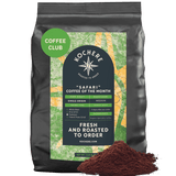A black bag of Kochere Coffee Company’s Safari "Coffee of the Month" Club—fresh roasted, single-origin coffee with a green label—sits next to ground coffee, highlighting freshness and ideal for any subscription or enthusiast.