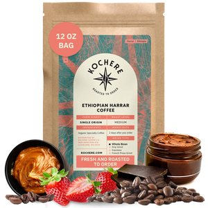A 12 oz bag of Kochere Coffee Ethiopian Harrar Natural Medium Roast by Kochere Coffee Company stands upright, surrounded by coffee beans, strawberries, chocolate pieces, and a jar of chocolate spread.[12 oz][Whole Bean]