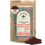 A bag of Kochere Coffee Ethiopian Harrar Natural Medium Roast by Kochere Coffee Company, featuring fruity blueberry and dark chocolate notes, sits beside fine ground coffee. The label shows origin, roast level, and freshness details.