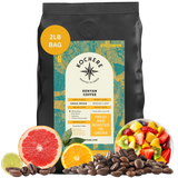 A 2lb bag of Kochere Coffee Kenyan Nyeri Embu AB by Kochere Coffee Company sits among fresh fruit, citrus slices, and coffee beans—highlighting the fruity, balanced, and bright notes of this medium-light roast.