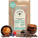 A bag of Kochere Coffee Ethiopian Sidamo Natural Medium-Light Roast sits among Sidamo coffee beans, chocolate, berries, and jars of swirling spreads.
