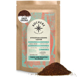 A 12oz bag of Kochere Coffee Ethiopian Sidamo Natural Medium-Light Roast by Kochere Coffee Company, featuring milk chocolate and fruity notes, with rich ground coffee piled in front of the package.[12 oz][drip grind]
