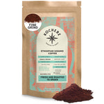 A 12oz bag of Kochere Coffee Company's Ethiopian Sidamo Natural Medium-Light Roast, with milk chocolate and fruity notes, is shown with aromatic grounds elegantly spilled in front.