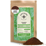 A brown bag of Kochere Coffee Company’s Organic Ugandan Sipi Falls Single Origin Medium Roast, featuring raisin, fig, and brown sugar notes, sits beside a pile of ground coffee, with a green label showing product details.[12 oz][drip grind]