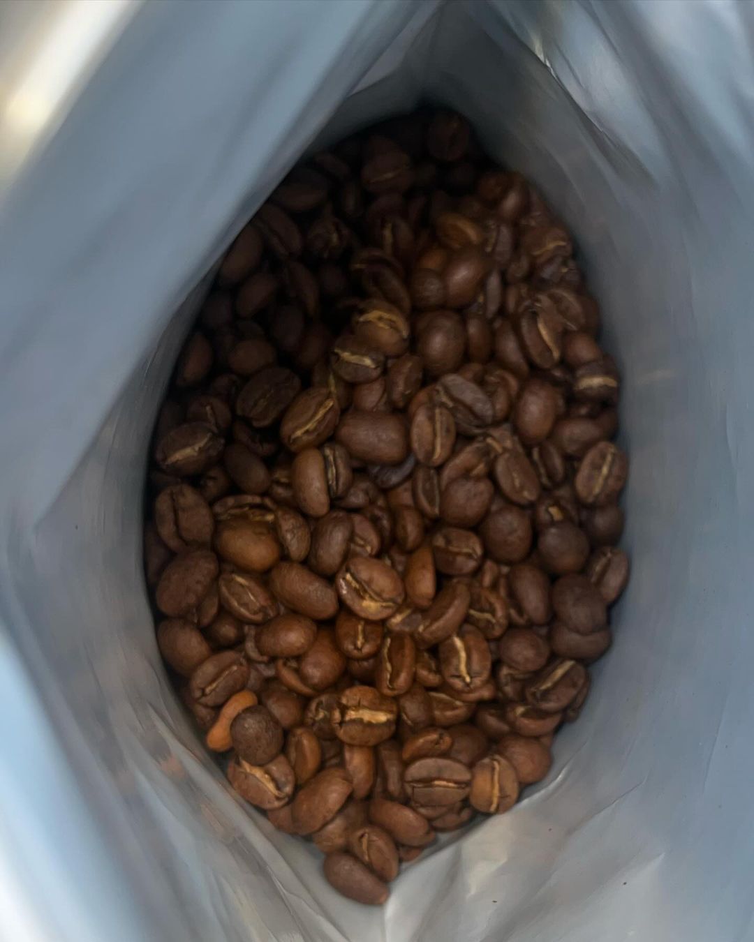 An open bag filled with medium-brown roasted coffee beans viewed from above.