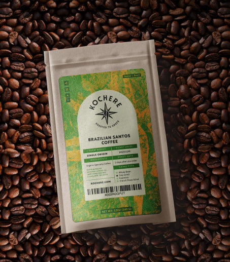 A bag of Kochere Brazilian Santos medium roast coffee sits on a surface covered with whole coffee beans.